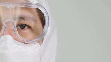 Koruyucu tehlikeli madde kıyafeti giyen Asyalı doktorun gözlerini kapat. Yüzü maske takıyor ve gözlük takıyor.