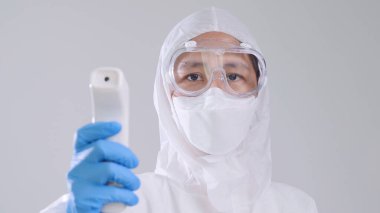 Kızılötesi termometreyle tarama yapan Asyalı tıp çalışanı kızıl ötesi termometreyle tarama yapan koruyucu PPE kostümlü ve gözlüklü kendine güvenen Asyalı doktor.