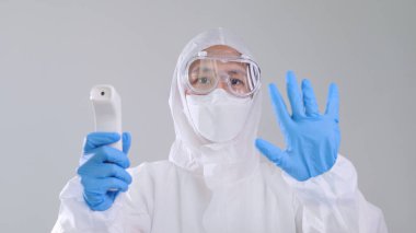 Kızılötesi termometreyle tarama yapan Asyalı tıp çalışanı kızıl ötesi termometreyle tarama yapan koruyucu PPE kostümlü ve gözlüklü kendine güvenen Asyalı doktor.