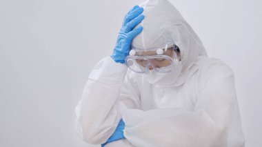 PPE takımlı stresli Asyalı doktor yerde oturuyor, çok çalışıyor.