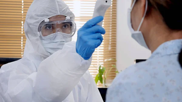 保護Ppeスーツのアジアの医師は 感染した女性患者の健康を確認するために赤外線温度計を使用して顔マスクや眼鏡を着用 — ストック写真