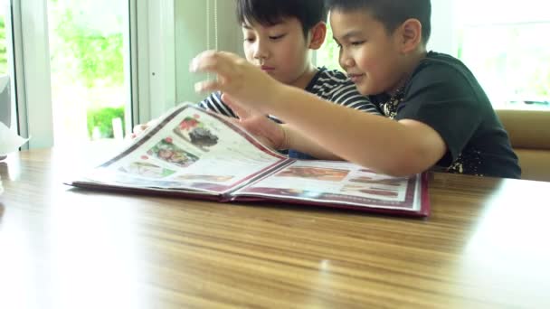 Gelukkig Aziatische kind zoeken en kies in menu boek. — Stockvideo
