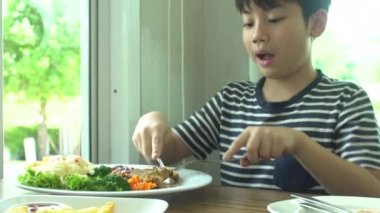 küçük Asyalı çocuk gülümsemek yüz ile restoranda sebze salatası ile Biftek yerken