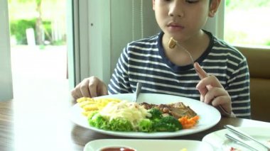 küçük Asyalı çocuk gülümsemek yüz ile restoranda sebze salatası ile Biftek yerken