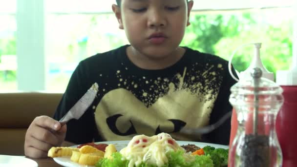 Pequeño asiático chico comer steak con vegetal ensalada en restaurante con sonrisa cara — Vídeos de Stock