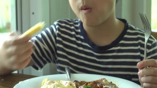 Азиатский мальчик ест стейк с овощным салатом в ресторане с улыбкой на лице — стоковое видео