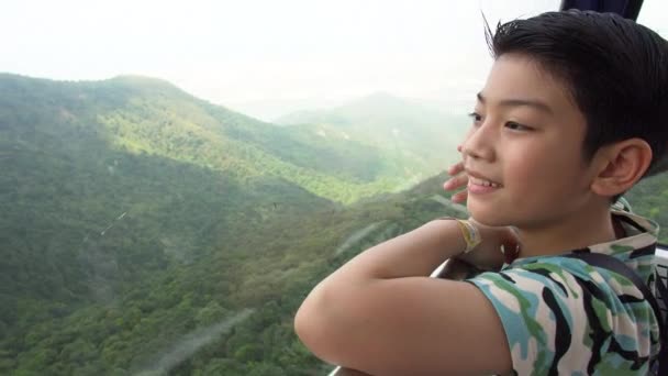 Счастливый азиатский мальчик в канатной дороге, глядя на холм природы — стоковое видео