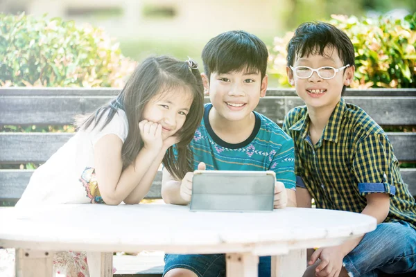 小小的亚洲女孩和男孩坐在长木椅子上，使用数字 — 图库照片