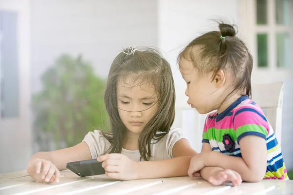 Två lite asiatisk tjej sitter på stol med hjälp av mobiltelefon — Stockfoto