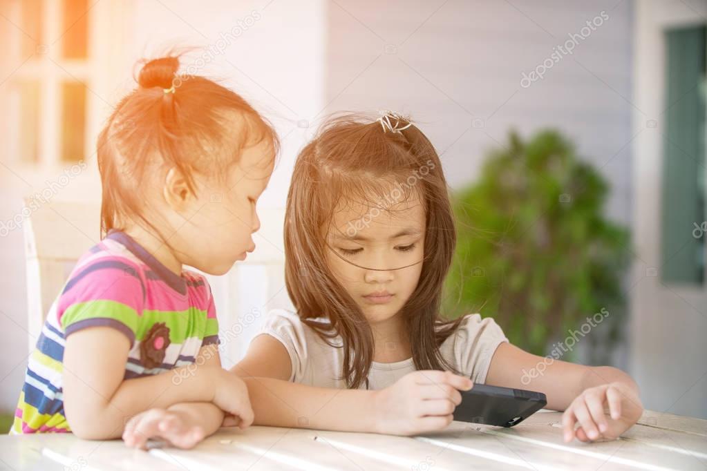 Two little asian girl sitting on chair using cell phone