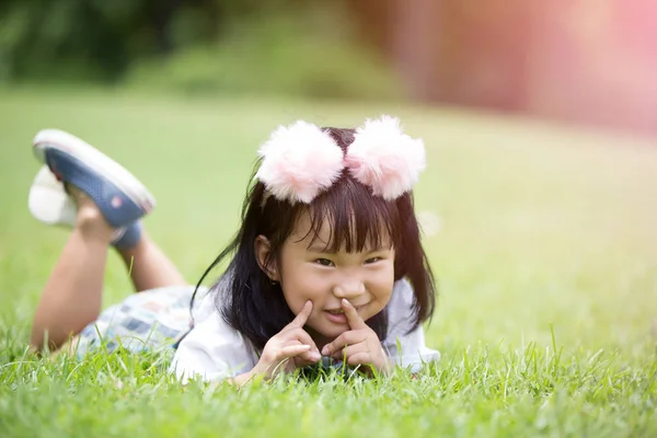 Pouco menina asiática jogando na grama verde no parque — Fotografia de Stock