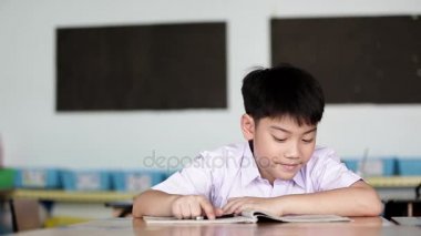 Asyalı çocuk okuma ve okulun ödevlerini yapmak yazma öğrenci üniforma .