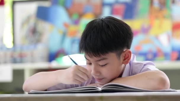 Niño asiático en uniforme de estudiante leyendo y escribiendo para hacer la tarea de la escuela  . — Vídeos de Stock