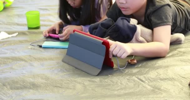 幸せなアジアの少年と少女再生スマート フォンとタブレットのキャンプ場で — ストック動画