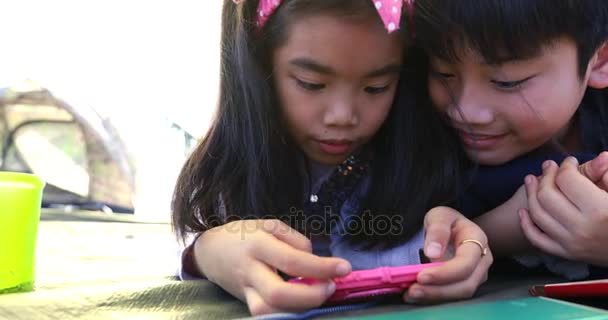 Счастливый азиатский мальчик и девочка играют в смартфон и планшет в кемпинге — стоковое видео