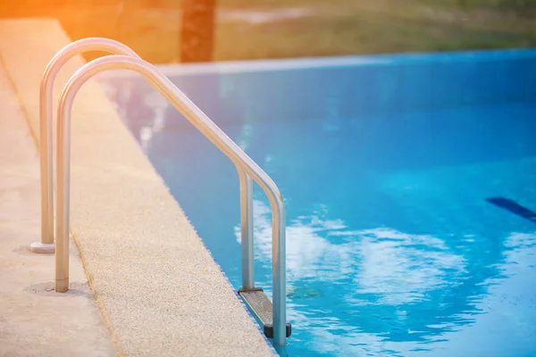 Haltestangen-Leiter im blauen Schwimmbad mit orangefarbenem Sonnenlicht — Stockfoto