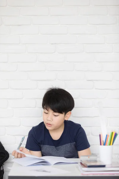 Ásia menino fazendo homework perto branco tijolo parede — Fotografia de Stock