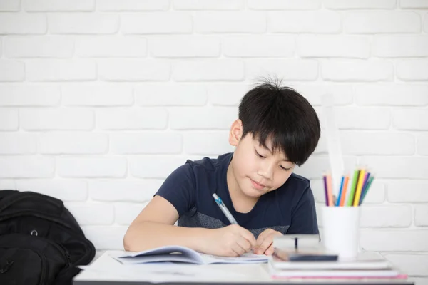 Ásia menino fazendo homework perto branco tijolo parede — Fotografia de Stock