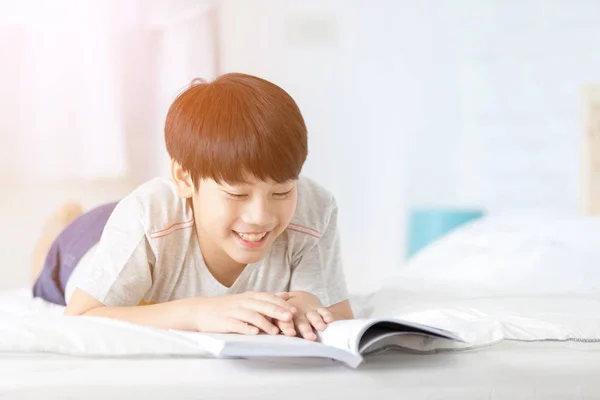 Feliz chico asiático leyendo libro de cuentos en la cama —  Fotos de Stock