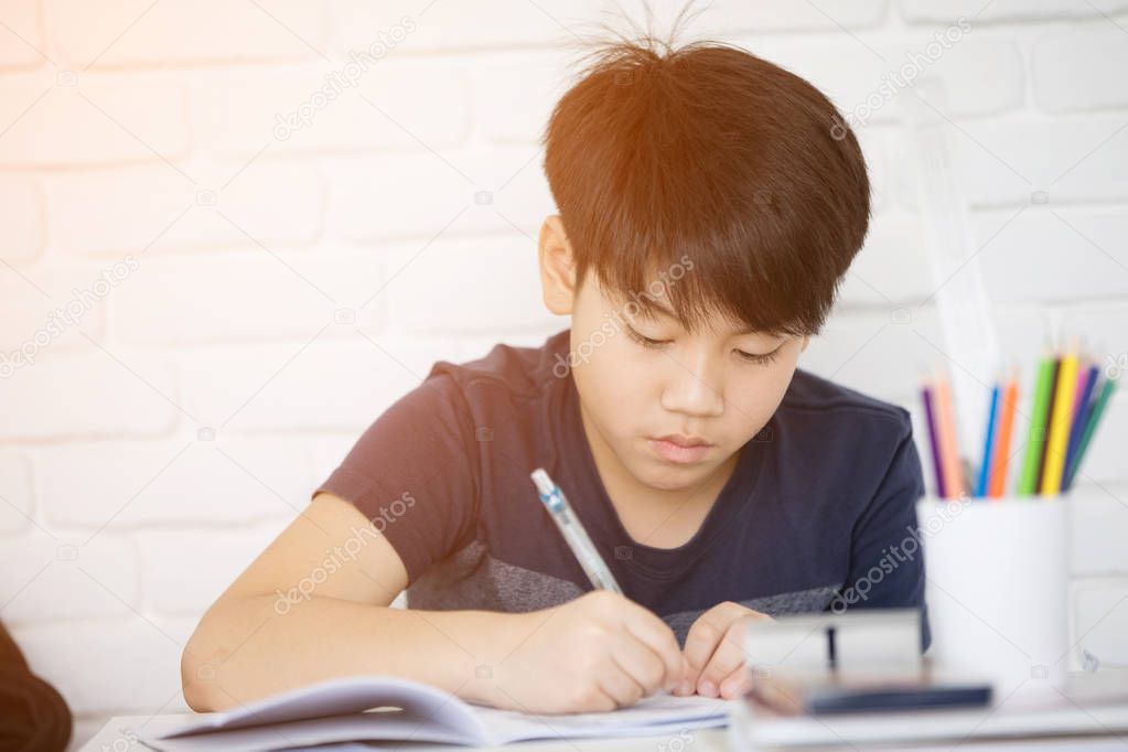 Asian boy doing homework near white brick wall