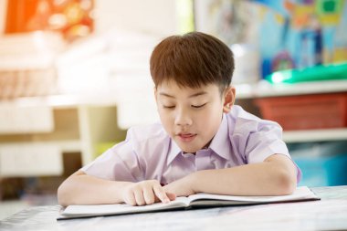 Mutlu Asyalı çocuk gülümsemek yüz okulda kitap okuma