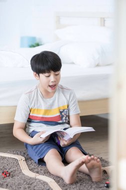 Asyalı çocuk sit h surata bir gülümseme ile zemin ve okuma kitabı