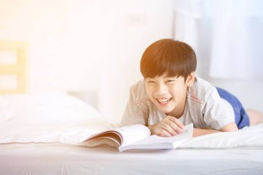 Asyalı çocuk dinlenme gülümsemek yüz yatak ve okuma kitabı