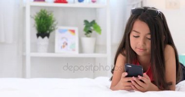 Mutlu Asya sevimli kız gülümsemek yüz evde ile akıllı telefon üzerinde oyun.