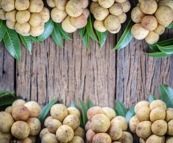 Langsat thailändsk frukt med gröna lämna på trä bakgrund, — Stockfoto