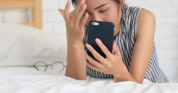 Linda mujer asiática sonriendo con su teléfono móvil en la cama hablando y mensajes de texto  . — Vídeo de stock