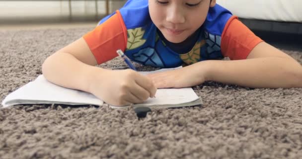 Lindo asiático chico resto en piso y hacer homework en casa con sonrisa cara . — Vídeos de Stock