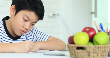 Sevimli Asya çocuk gülümsemek yüz ile evde ödev yapmak.
