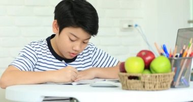 Sevimli Asya çocuk gülümsemek yüz ile evde ödev yapmak.