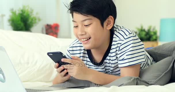 可爱的亚洲男孩手里拿着智能手机和打字机与微笑的脸. — 图库视频影像