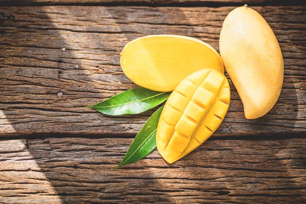 Zralé mango nakrájené na zalesněné desce se zelenými listy. — Stock fotografie
