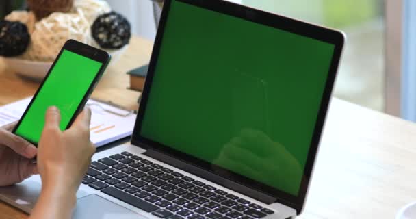 Азиатская женщина держит сотовый телефон. Телефон и ноутбук на столе с зеленым экраном . — стоковое видео