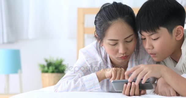 Mutlu Asya ailesi kız kardeşi ve cep telefonu yatağın üzerine oynayan kardeşi. — Stok video