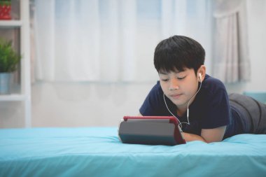 Sevimli Asya çocuk dinlenme yatak ve tablet bilgisayar tutan el. 