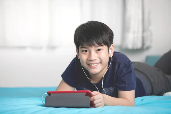 Bonito ásia menino resto no cama e mão segurando tablet computador . — Fotografia de Stock