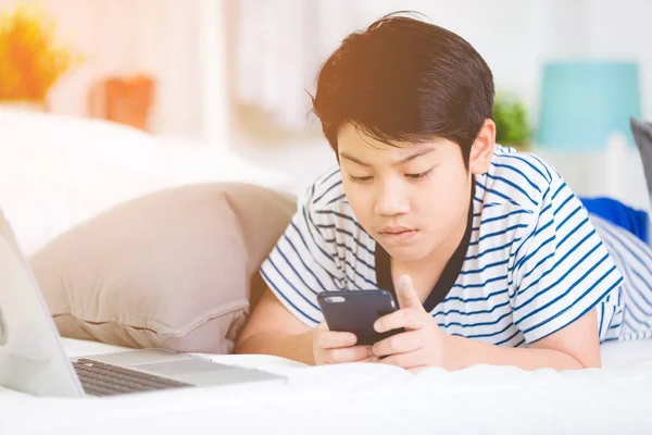 Lindo asiático chico resto en cama y usando inteligente celular con sol l —  Fotos de Stock