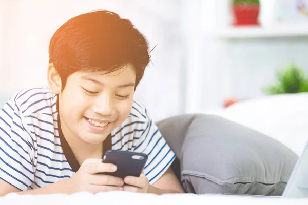 かわいいアジアの男の子残りのベッドとスマート携帯電話を使用して. — ストック写真