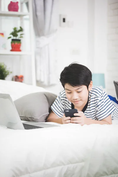 Bonito ásia menino resto no cama e usando inteligente celular . — Fotografia de Stock