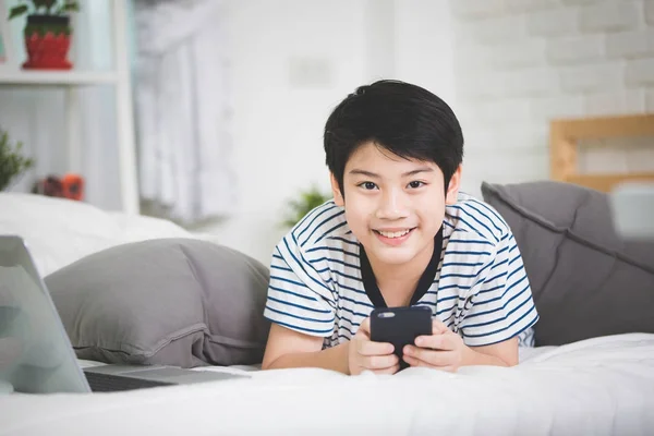 Sød asiatisk dreng hvile på seng og hånd holder tablet computer . - Stock-foto