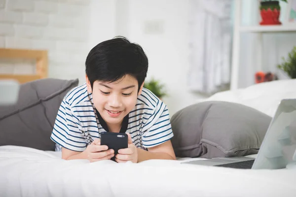 Cute asian boy rest on bed and using smart cell phone . — Stock Photo, Image