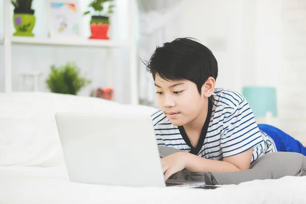Lindo asiático chico resto en cama y mecanografía laptop ordenador . —  Fotos de Stock
