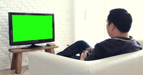 Rückansicht asiatischer Mann spielt Computerspiel mit grünem Bildschirm im Fernsehen.