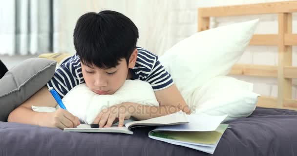 アジアの少年の自宅のベッドの上の友人の残りの部分の宿題をして 本を読んで — ストック動画