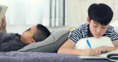 Asyalı çocuk evde yatakta arkadaş geri kalanı ile ödev ve kitap okuma .