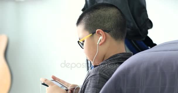 技术和人的概念 微笑的亚洲男孩与智能手机和耳机听音乐或在家里玩游戏 — 图库视频影像