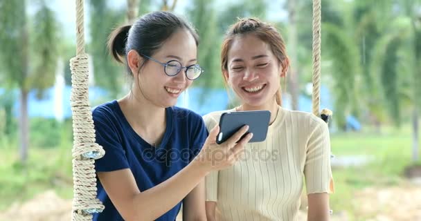 幸せなアジアの家族の姉と妹は笑顔でスイング椅子に携帯電話を保持している手 — ストック動画